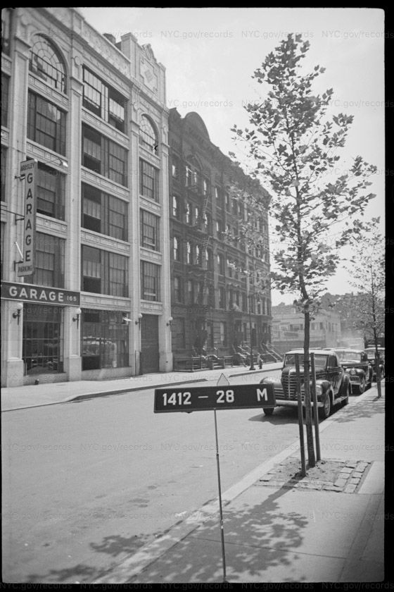 Tax photograph of a light-coloured commercial building with tall multi-pane windows, a fascia sign reading GARAGE 165 and a vertical blade sign reading GARAGE PARKING, standing next to the same row of dark brick tenements.