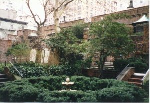 Colour snapshot of a circular hedge enclosing a small fountain, with bare trees, ivy-covered brick walls and the Regency rear of the Cottages behind.